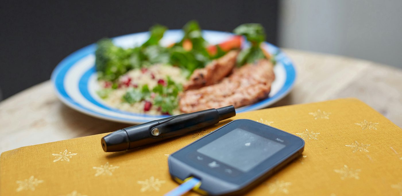 Glucose meter and test pen beside a healthy plate of food